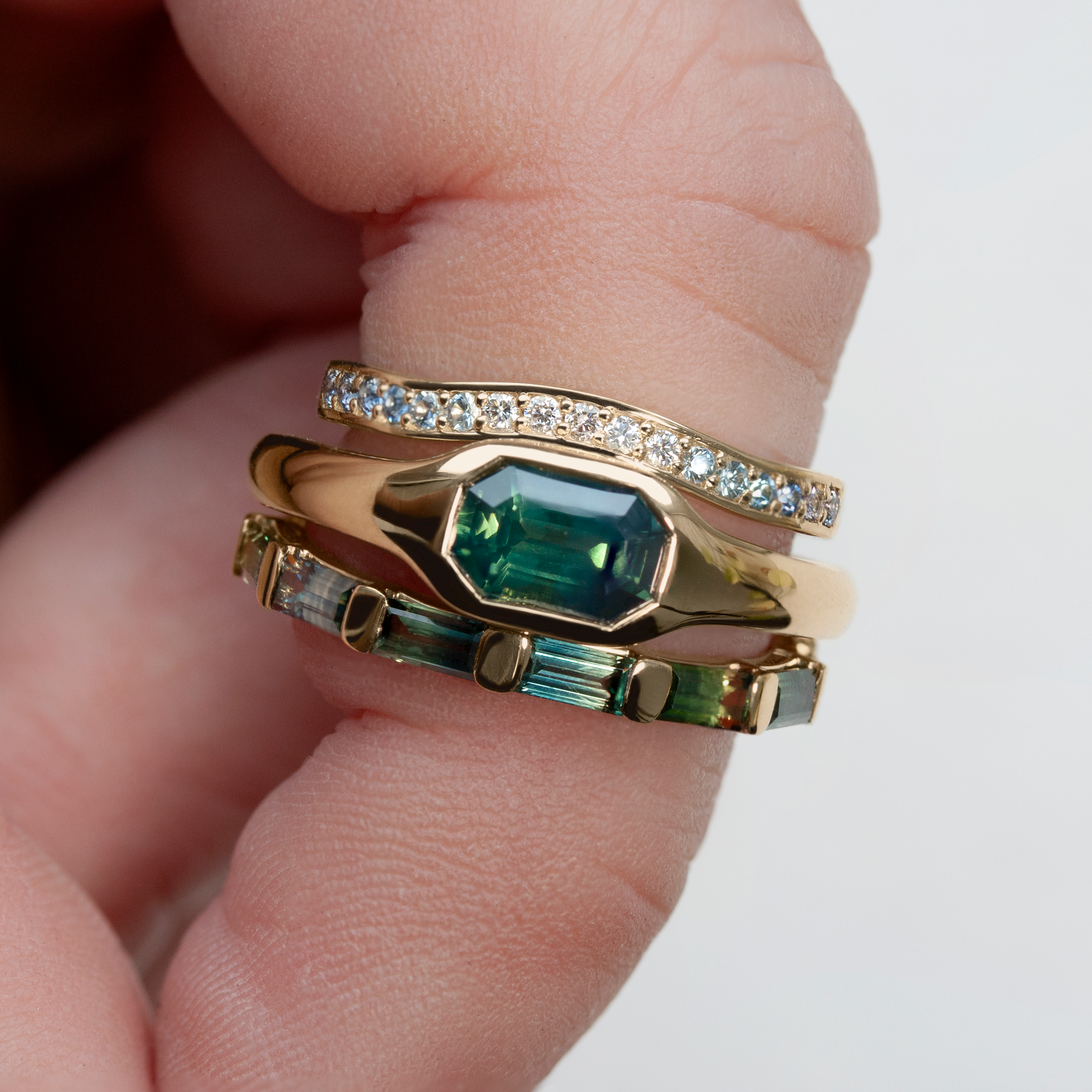 Gold signet ring by Philadelphia local jeweler Emily Chelsea Jewelry, featuring a green emerald center stone, soft curves, and paired with extra bands.