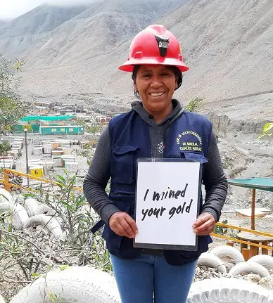 Woman near a mine holding a sign that says "I mined your gold"