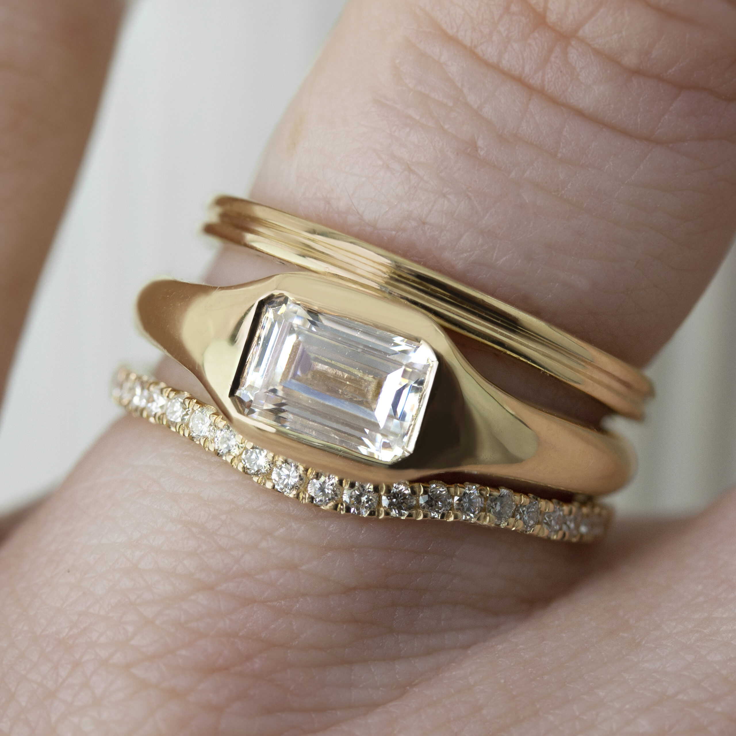 Emerald-cut gold signet ring by Philadelphia's Emily Chelsea Jewelry, worn with bands, featuring soft curves and a flush-set center stone.