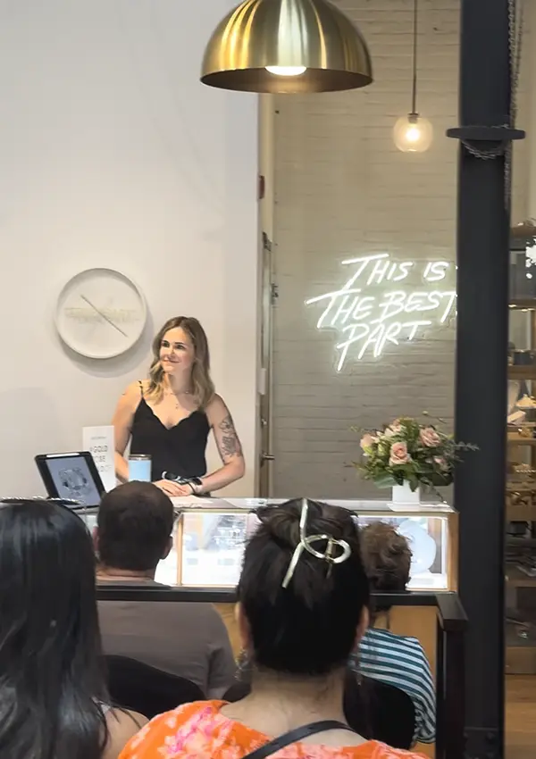 A woman stands in front of a team of jewelers in an office