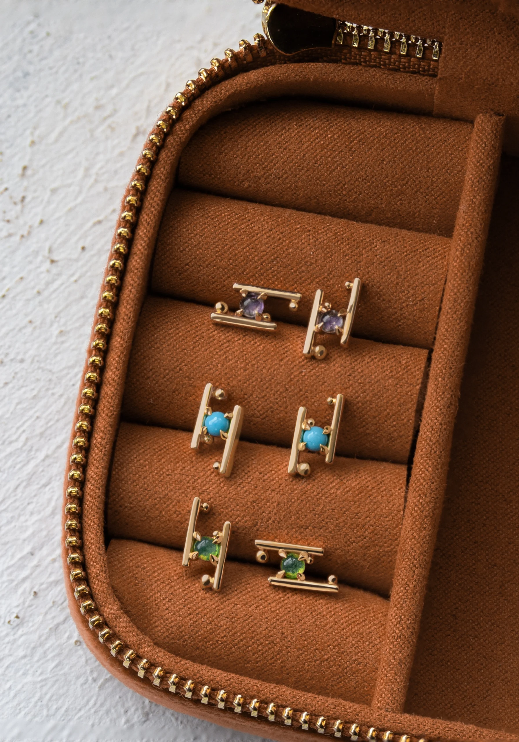 A jewelry box holding gold earrings with amethyst, turquoises and moss agate gems