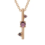 The Through It All Necklace by Emily Chelsea Jewelry features a metal bar motif symbolizing resilience, with Indian moss agate and Nigerian green tourmaline. Custom design.